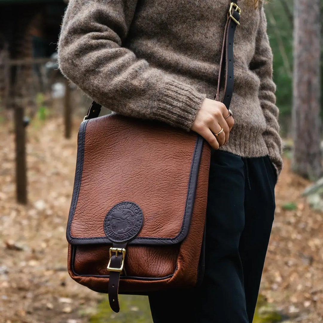 Woman in a sweater wearing a Duluth Pack Bison Leather Haversack with a forest in the background. 