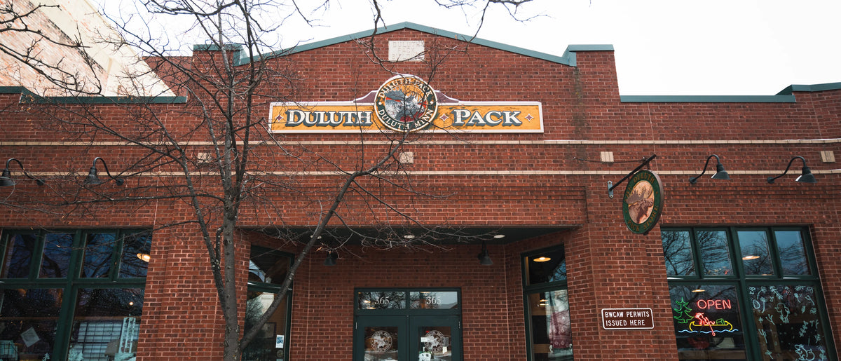 Historic Duluth Pack storefront with vintage brick exterior, classic signage, and large windows, reflecting a heritage of handmade outdoor canvas and leather gear since 1882.